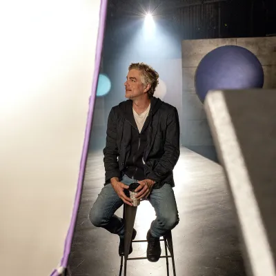 Hubert Proulx assis sur un tabouret, sur le plateau de tournage de la série Nos géants, saison 3